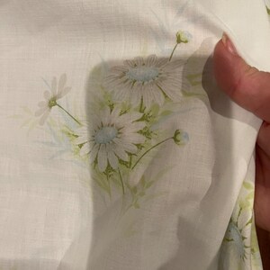 May include: White fabric with a light blue and green floral pattern. The fabric has a subtle linen texture.