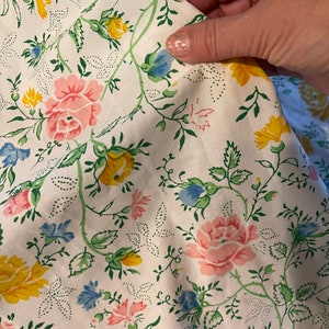 May include: White fabric with a floral pattern featuring pink, yellow, and blue flowers on green vines. The fabric has a white background with small white dots.
