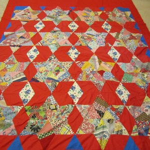 May include: A red quilt with a blue border. The quilt is made of many different fabrics in a variety of colors and patterns. The quilt is made in a star pattern.