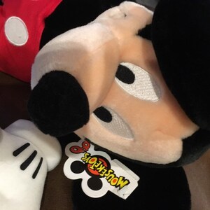 May include: A black and white plush Mickey Mouse toy with a red shirt and a white tag that says "MousekeToys".