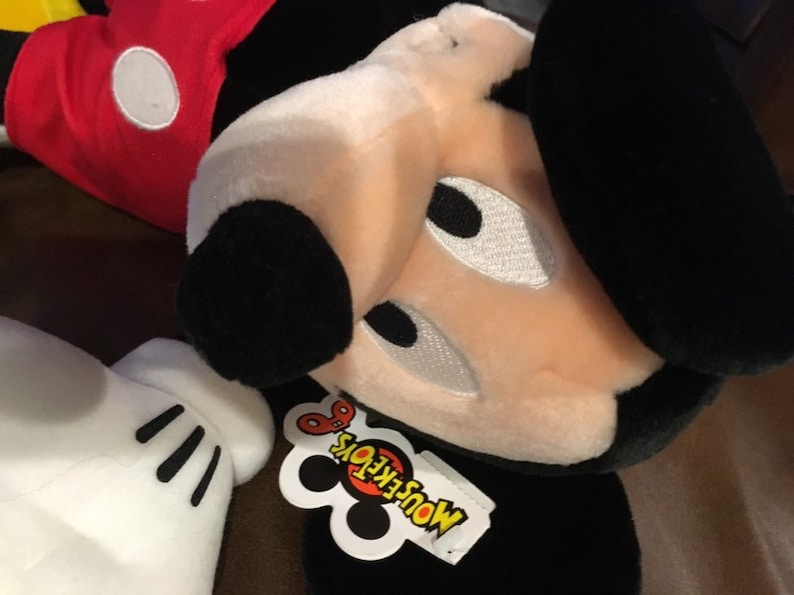 May include: A black and white plush Mickey Mouse toy with a red shirt and a white tag that says "MousekeToys".