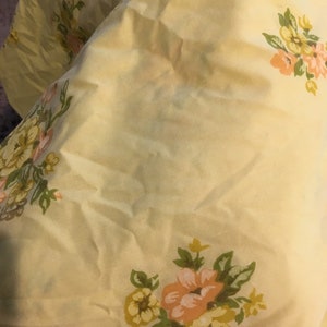 May include: A yellow fabric with a floral pattern. The flowers are pink, yellow, and green.