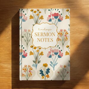 Peut inclure: Un carnet à couverture rigide avec un fond crème orné d'un motif répétitif de fleurs stylisées dans des tons rose, jaune et bleu. Une étiquette centrale blanche à bordure dorée affiche le texte "lindsey's SERMON NOTES" en lettres dorées.