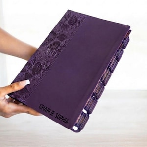 May include: A deep purple journal featuring a textured floral embossed pattern along the left side and the name CHARLIE SOPHIA printed in black on the front cover. The book includes multiple dark purple index tabs extending from the right edge.