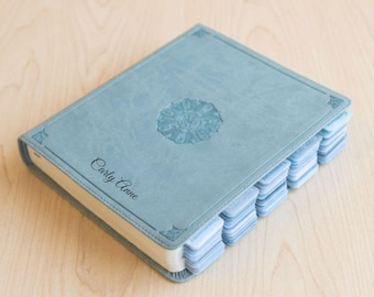 Könnte beinhalten: Hellblaues Notizbuch mit floralem Prägemuster auf dem Einband. Das Notizbuch trägt die Inschrift "Carly Anne". Es hat mehrere Seitenregister.