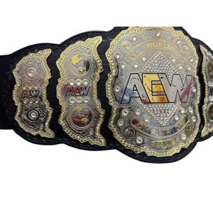 Könnte beinhalten: Ein Wrestling-Meisterschaftsgürtel mit einem schwarzen Lederriemen und goldenen und silbernen Metallplatten. Die zentrale Platte trägt die Buchstaben "AEW" und die Worte "WORLD CHAMPION" und "PAYNE".