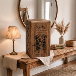 Puede incluir: Una urna rectangular de madera para mascotas con acabado marr&oacute;n oscuro. El frente presenta un retrato grabado de un perro, el nombre Rocky, el texto Thank you for the love and joy y los a&ntilde;os 2013-2024. El panel lateral muestra huellas de patas.