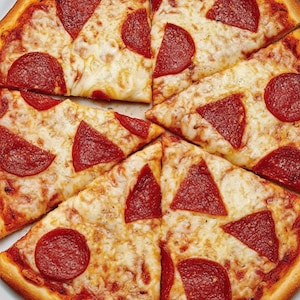 Puede incluir: Primer plano de una pizza de pepperoni en rodajas. La pizza tiene una corteza dorada, queso derretido y rodajas redondas de pepperoni. La pizza está cortada en porciones triangulares, lista para comer.