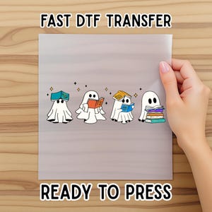 May include: A sheet with the text "FAST DTF TRANSFER" and "READY TO PRESS" featuring four cartoon ghosts reading books. The ghosts are white with black eyes and are holding books of various colors. The sheet is held by a person.