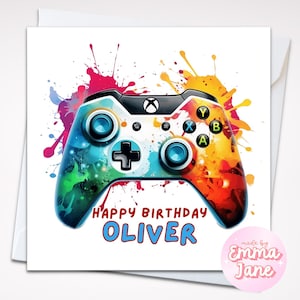 Puede incluir: Tarjeta de felicitación con un diseño colorido de mando de Xbox sobre un fondo de salpicaduras de acuarela. El texto "Happy Birthday Oliver" está en la tarjeta. La tarjeta tiene un sobre blanco y una pegatina rosa que dice "made by Emma Jane".