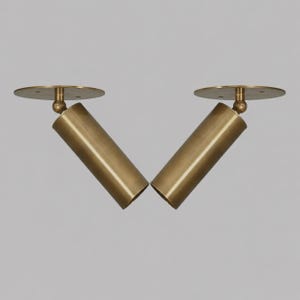 May include: Two brass-colored, cylindrical spotlights with circular mounting plates. The spotlights are angled, creating a V-shape. The design is minimalist and modern, suitable for interior lighting.