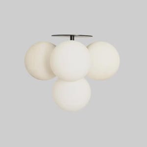 Peut inclure: Un plafonnier moderne avec quatre abat-jours sphériques en verre blanc cassé. Les abat-jours sont regroupés et fixés à une base en métal noir avec une plaque circulaire. Le luminaire est conçu pour une utilisation en intérieur.