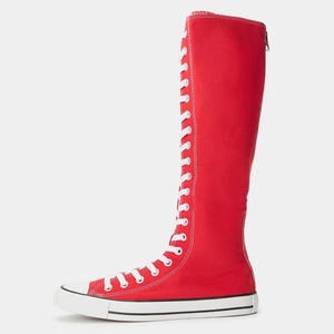 Puede incluir: Una bota alta roja de lona con un cierre frontal de cordones blancos que se extiende desde la punta hasta la parte superior de la ca&ntilde;a. La bota incluye una puntera de goma blanca, una entresuela blanca con una fina raya negra y una cremallera en la parte posterior.