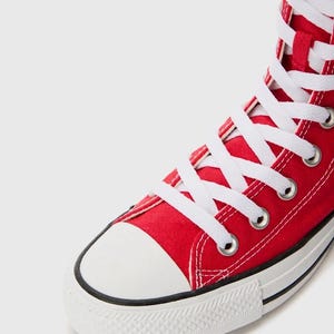 Puede incluir: Una zapatilla alta de lona roja brillante con cordones blancos, ojales met&aacute;licos plateados, puntera de goma blanca y suela de goma blanca con una fina raya negra a lo largo del borde de la construcci&oacute;n de la entresuela.