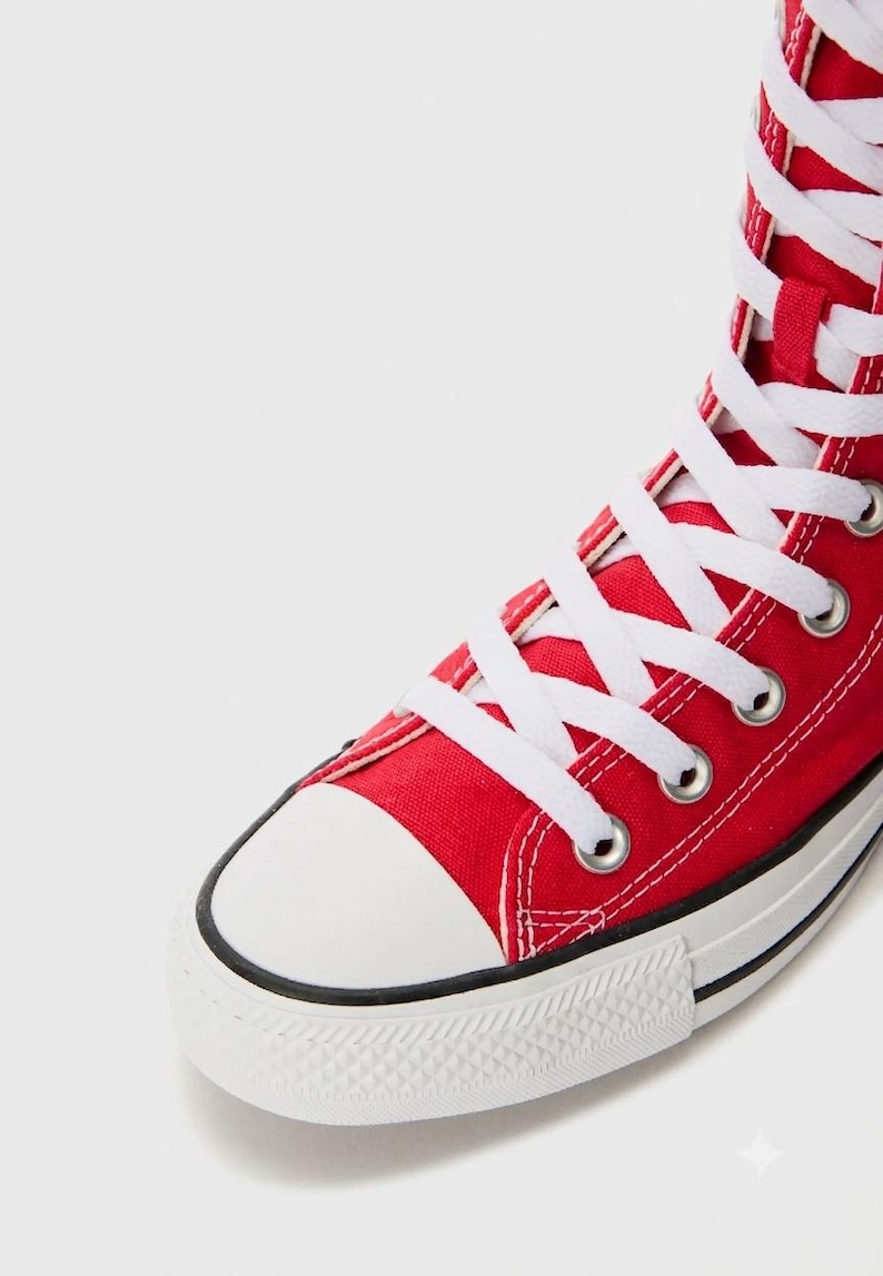 Puede incluir: Una zapatilla alta de lona roja brillante con cordones blancos, ojales met&aacute;licos plateados, puntera de goma blanca y suela de goma blanca con una fina raya negra a lo largo del borde de la construcci&oacute;n de la entresuela.
