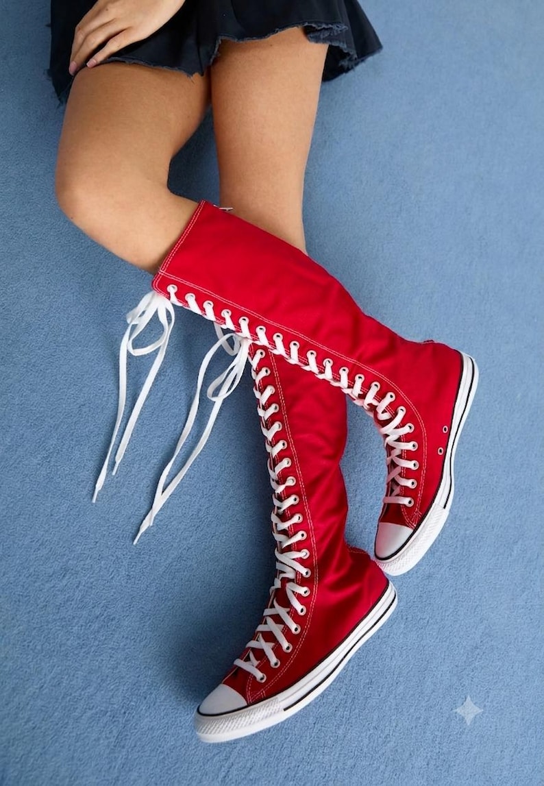 Puede incluir: Un par de zapatillas de lona rojas hasta la rodilla con un dise&ntilde;o de cordones de arriba a abajo, cordones blancos, punteras de goma blanca y suelas de goma blanca con ribetes negros. Las botas cubren la parte inferior de la pierna.