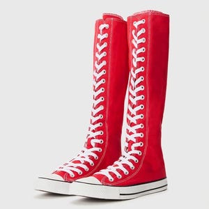 Puede incluir: Un par de zapatillas de lona rojas hasta la rodilla con una ca&ntilde;a alta, cordones blancos que recorren toda la parte delantera, punteras de goma blanca y suelas de goma blanca con un fino detalle de raya negra en el borde de la base.