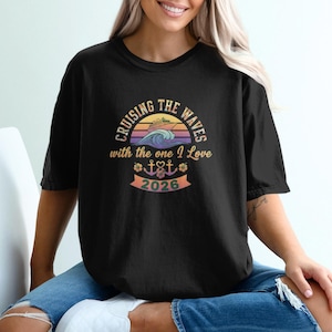 May include: Black t-shirt featuring the text "Cruising the Waves with the one I Love" in a circular design with a ship and waves. The design also includes the year "2026". The shirt is a casual style.