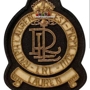 Puede incluir: Parche bordado en negro y dorado con el texto "LAUREN" y "RL". El parche tiene un borde dorado y una corona dorada en la parte superior. También es visible el texto "EMPIRE LAUREN ET FICH".
