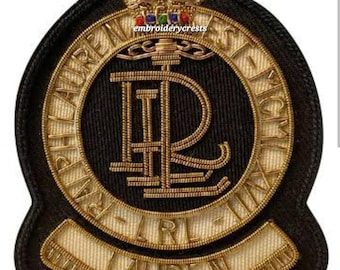 May include: A black and gold embroidered patch with the text "LAUREN" and "RL". The patch has a gold border and a gold crown at the top. The text "EMPIRE LAUREN ET FICH" is also visible.