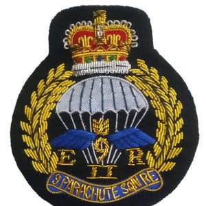 Op de afbeelding: Geborduurde patch met een gouden kroon, parachute en vleugels op een zwarte achtergrond. De patch bevat de tekst "ER II" en "9 PARACHUTE SQN RE". Het ontwerp is gedetailleerd met gouden, blauwe en zilveren draad.