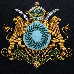 May include: Embroidered emblem featuring a central light blue shield with a green wreath, flanked by two golden lions. A detailed crown sits above, with decorative elements in red, green, and white. The background is black.
