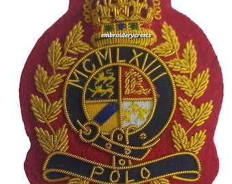 May include: A red embroidered patch with gold detailing. The patch features a crown, laurel leaves, and a circular emblem with the text "MCMLXVII". A banner at the bottom reads "POLO".