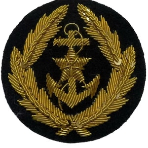 Op de afbeelding: Een cirkelvormige zwarte patch met een gouden ankerembleem, omringd door een gouden laurierkrans. Het anker en de krans zijn fijn geborduurd met gouddraad, wat een textuur geeft. De patch is waarschijnlijk een militair of nautisch insigne.