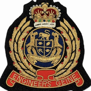 May include: A black embroidered patch featuring a gold crown, laurel leaves, and a blue and gold emblem with two lions and a shield. The red banner at the bottom reads "ENGINEERS GEINE".