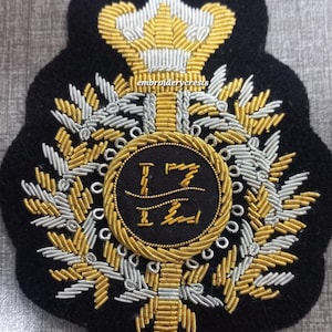 Könnte beinhalten: Schwarzer gestickter Aufnäher mit goldenen und silbernen Metallic-Garn-Details. Der Aufnäher zeigt eine Krone, Lorbeerblätter und ein zentrales rundes Emblem mit Text. Der Text "embroiderycrests" ist sichtbar.