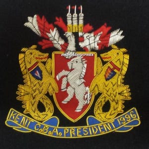 Può includere: Stemma ricamato su sfondo nero. Lo stemma presenta uno scudo rosso con un cavallo bianco, affiancato da creature dorate simili a cavallucci marini. Il testo include "KENT C.B.O.A. PRESIDENT 1996" in blu.