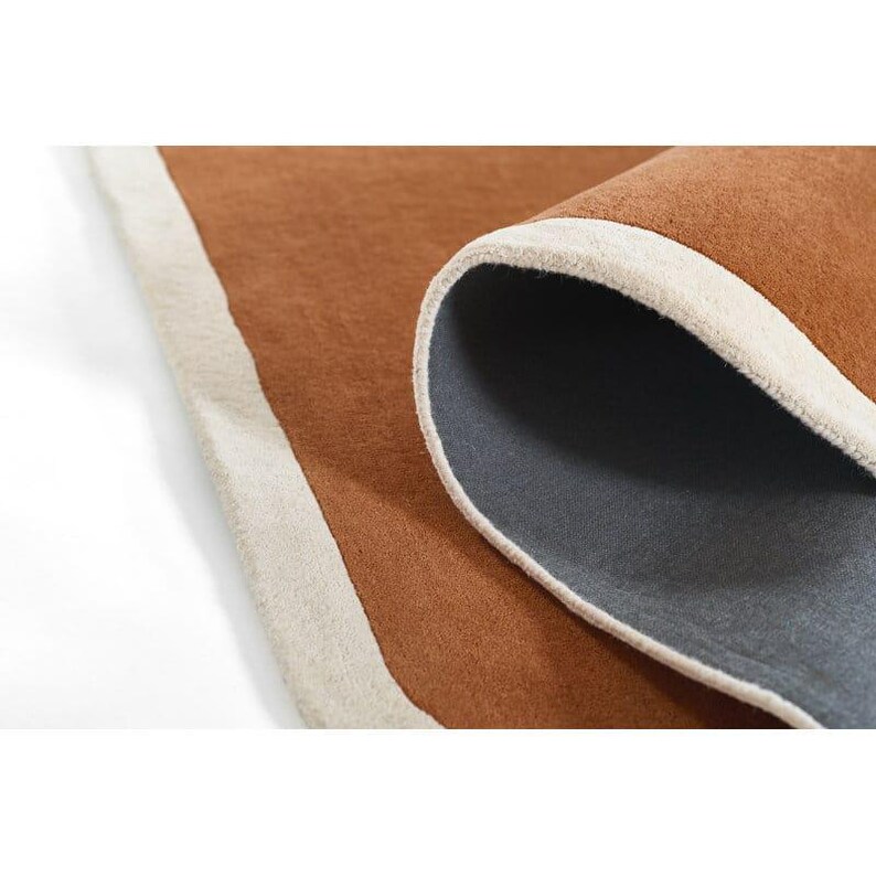 May include: A rolled-up brown rug with a cream-colored border. The underside of the rug is a dark gray color. The rug is made of a soft, textured material.