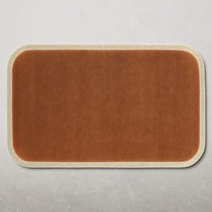 May include: A rectangular, rust-colored rug with rounded corners and a cream-colored border. The rug has a soft, textured appearance, suitable for a living room or bedroom. The rug's dimensions are not visible.