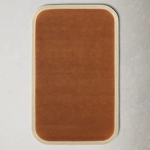 May include: A rectangular rug with rounded corners. The rug has a solid, warm brown center and a cream-colored border. The rug's design is simple and modern, suitable for various interior styles. The rug is likely made of a soft, durable material.
