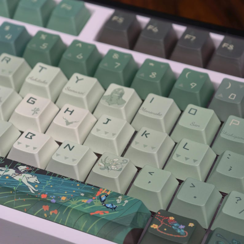 May include: Close-up of a mechanical keyboard with custom keycaps. The keycaps are a mix of green and off-white, with various symbols and Japanese characters. The space bar features a detailed illustration of a forest scene with butterflies.