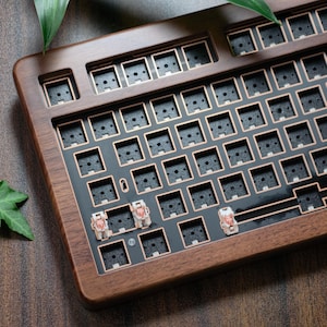 Puede incluir: Base de teclado de madera con acabado marrón oscuro. El teclado tiene una placa negra con contornos de interruptores de color cobre. Algunos interruptores están instalados. Diseñado para la personalización.