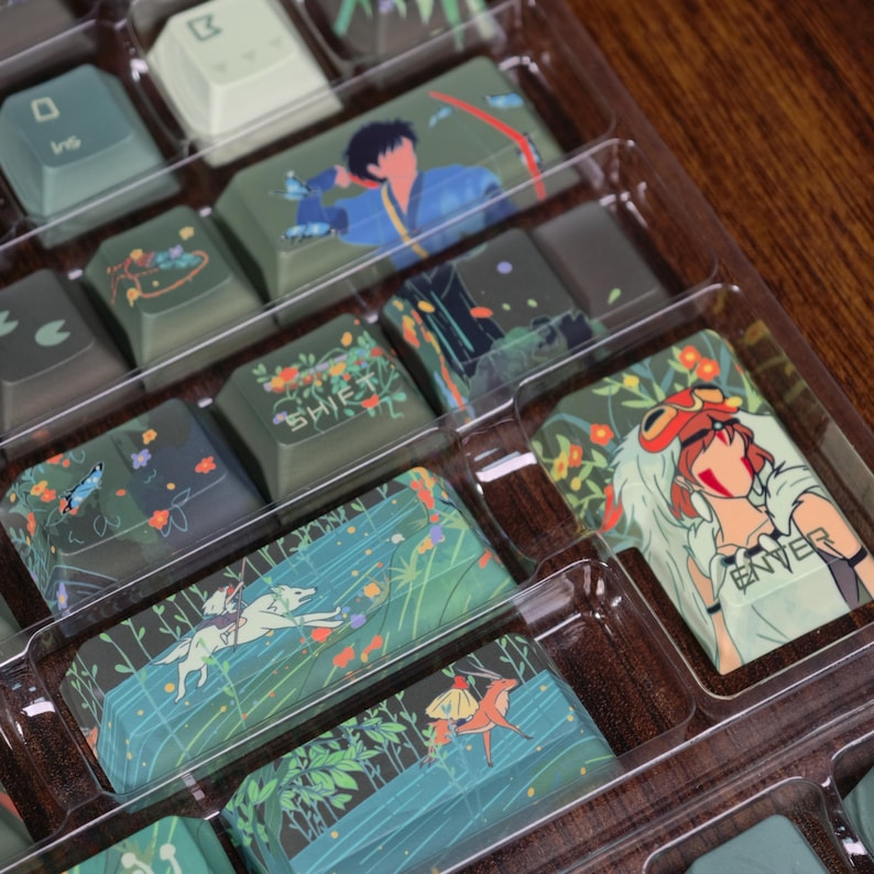 May include: A set of custom keycaps with various designs, including illustrations of characters and scenes. The keycaps feature a mix of colors, including green, blue, and white, and are packaged in a clear plastic tray.