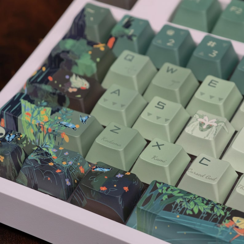 May include: A custom mechanical keyboard with green and dark teal keycaps. Some keycaps feature illustrations of butterflies, flowers, and forest scenes. The keyboard has a white frame and a variety of letter and number keys.