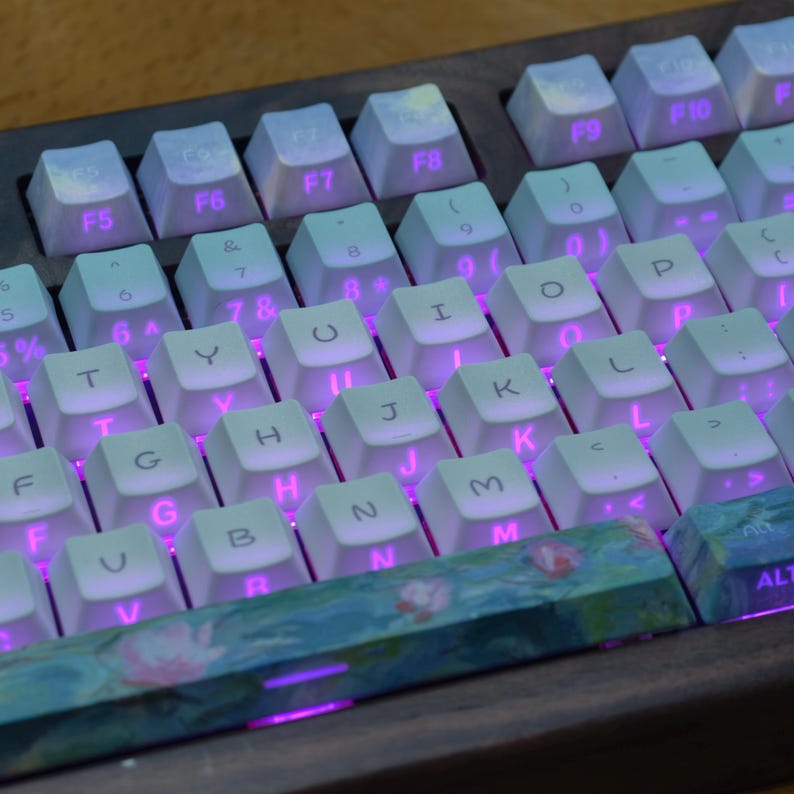 May include: A mechanical keyboard featuring white keycaps with black lettering and vibrant purple backlighting. The spacebar and bottom row keys display a colorful floral pattern. The keyboard is set within a dark wooden frame.