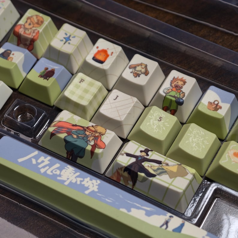 May include: A set of custom keyboard keycaps featuring various anime-style illustrations. The keycaps have a light green and white color scheme, with images of characters and objects. The spacebar has Japanese text and a light green and blue design.