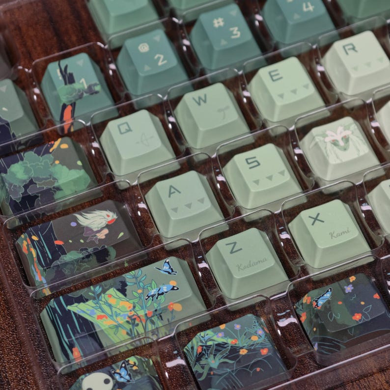 May include: A set of custom keycaps in a clear plastic tray. The keycaps are primarily light green with various designs, including floral patterns, butterflies, and stylized illustrations. Some keycaps have letters and numbers.