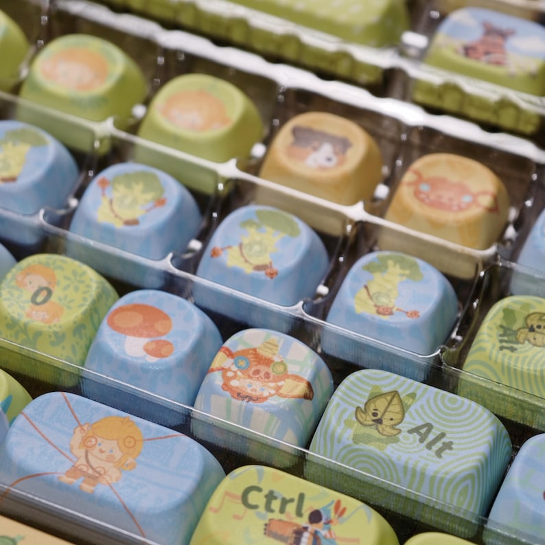 Puede incluir: Primer plano de un recipiente de pl&aacute;stico transparente lleno de bombones cuadrados de colores. Cada bomb&oacute;n est&aacute; decorado con un gr&aacute;fico de dibujos animados diferente, incluyendo una jirafa, una seta y los textos "Alt" y "Ctrl". Los bombones son azules, verdes y amarillos.
