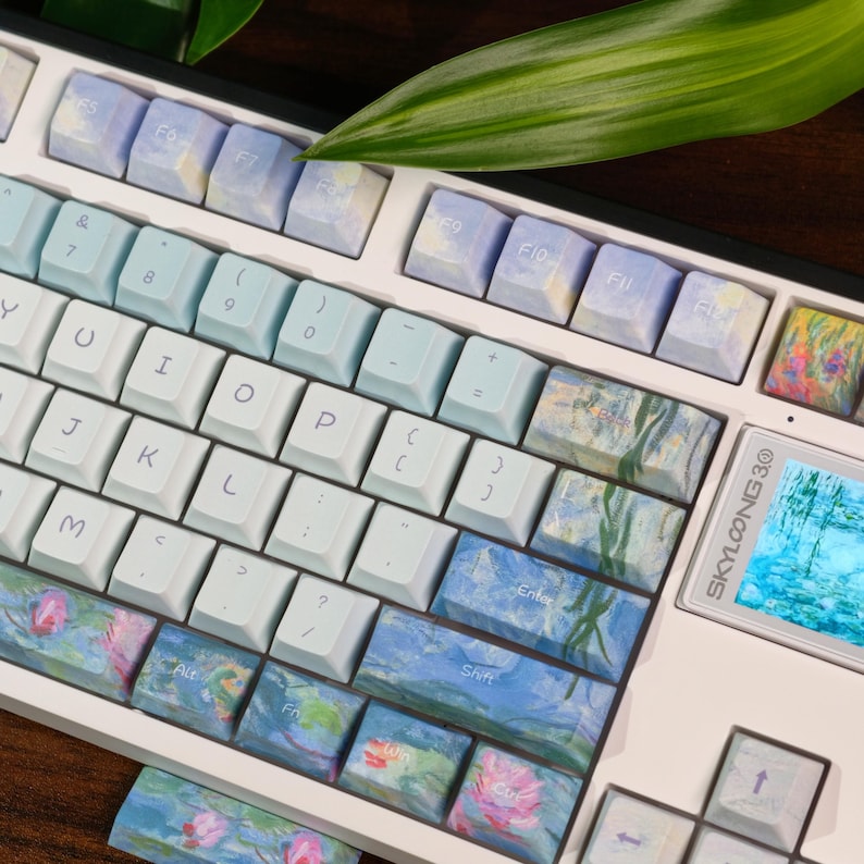 May include: A mechanical keyboard with a white frame featuring custom keycaps. The keys display a mix of solid light blue and artistic impressionist-style floral patterns. A small digital screen on the right side displays the text SKYLOONG.