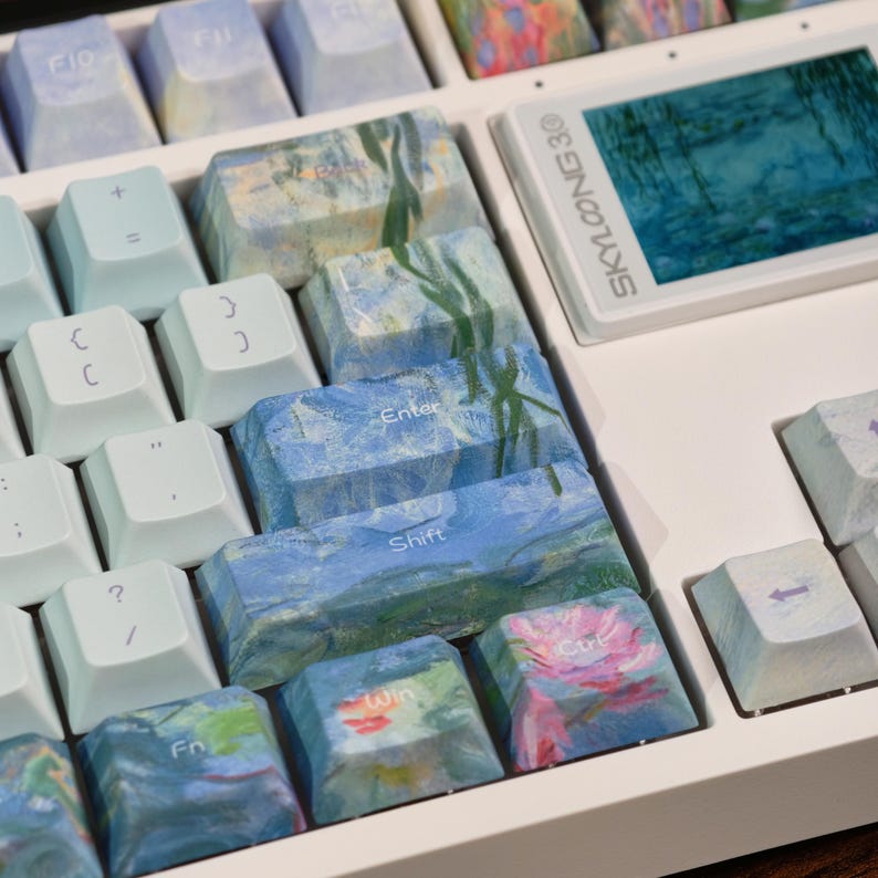 May include: A white mechanical keyboard featuring custom keycaps with impressionist-style floral and water lily paintings in shades of blue, green, and pink. The keyboard includes a small rectangular screen displaying the text SKYLOONG 30.