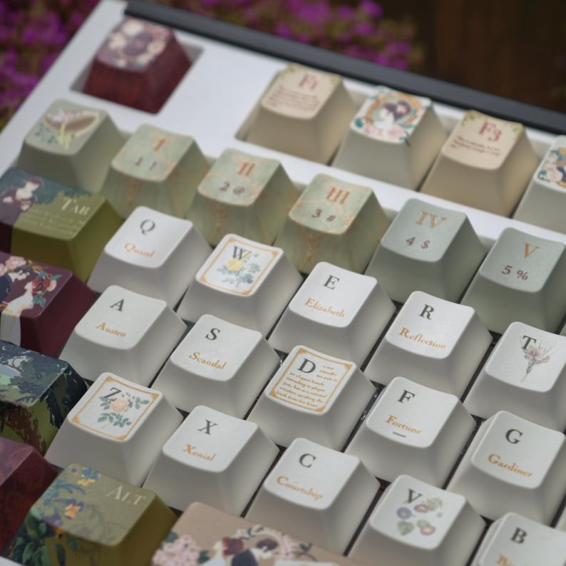 May include: A custom keyboard with keycaps featuring literary themes. The keycaps are off-white with various designs, including floral motifs, book titles, and quotes. The keyboard has a white frame and a selection of keycaps with different colors.