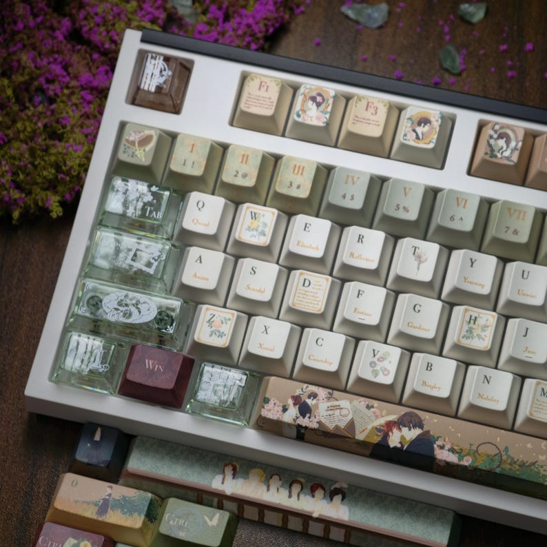 May include: A custom keyboard with a white frame and keycaps featuring various designs and illustrations. The keycaps have a beige and green color scheme, with some keys displaying text and images. The keyboard is set against a blurred background with purple flowers.