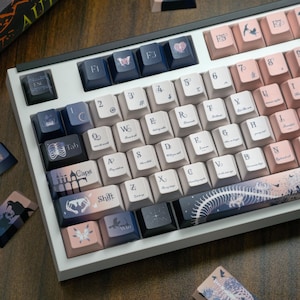 May include: A custom mechanical keyboard with a white frame and keycaps in shades of blue, pink, and white. The keycaps feature various illustrations, including butterflies, birds, and anatomical designs. The keyboard has a unique aesthetic.