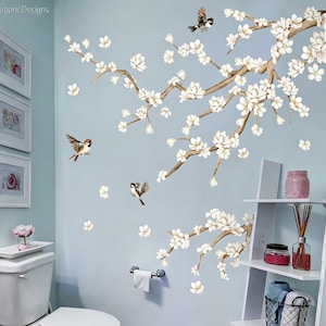 May include: Wall decal featuring a blossoming tree branch with white flowers and small birds in flight. The design is set against a light blue wall, creating a serene and natural aesthetic. Decorative wall art.