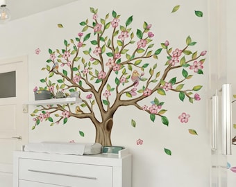 May include: A wall decal featuring a large tree with brown branches, green leaves, and pink blossoms. Several small birds are perched on the branches. The decal is applied to a white wall, with a white dresser and shelf visible below. The text "SunoneDesigns" is in the upper right corner.
