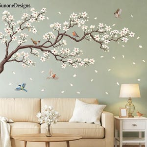 May include: Wall decal featuring a blossoming tree branch with white flowers and several birds in flight. The decal includes falling petals and is set against a light green background. The brand name "SunoneDesigns" is in the top left corner.